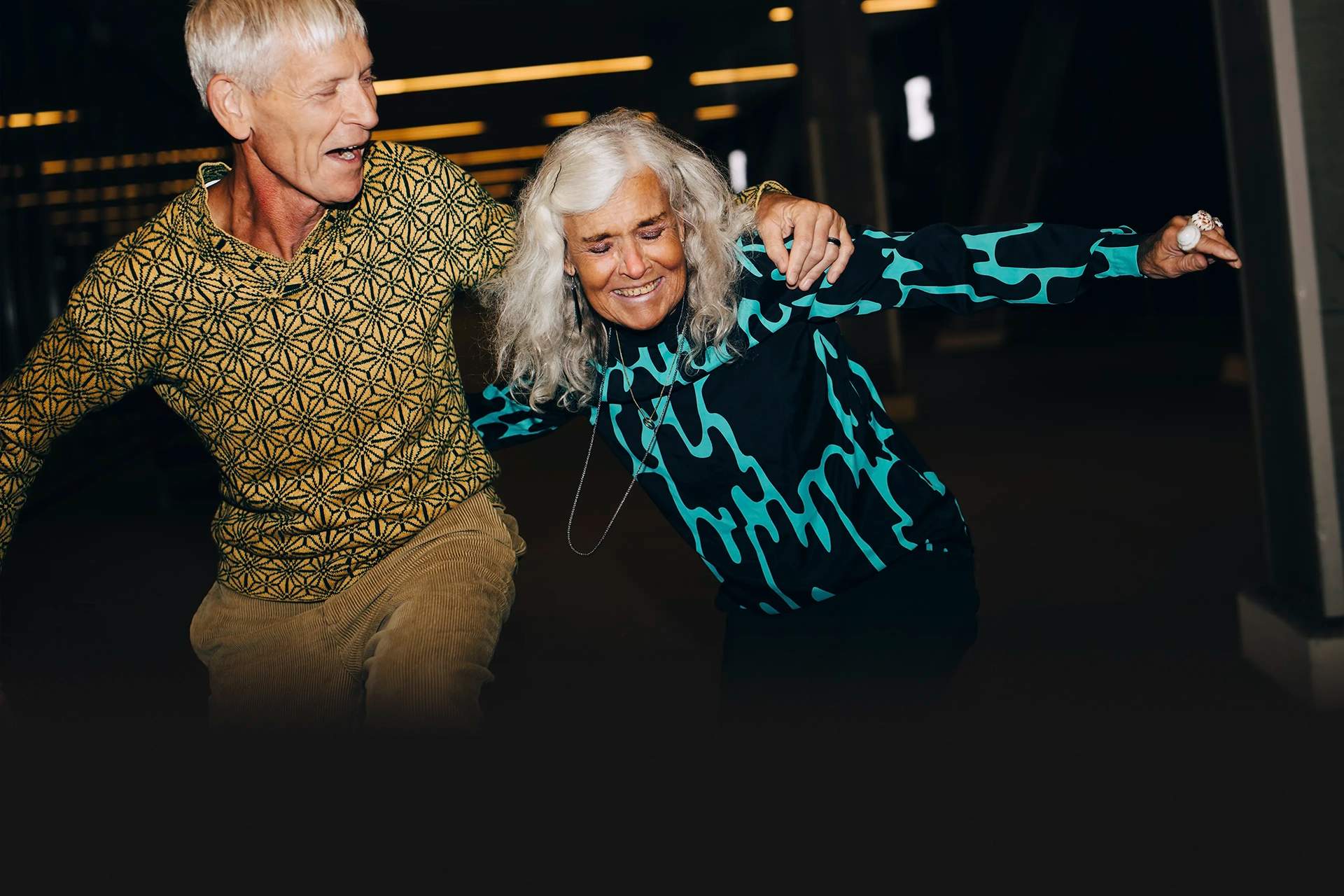 A photo of a man and woman both with white hair, with their arms around each other, smiling and having fun.