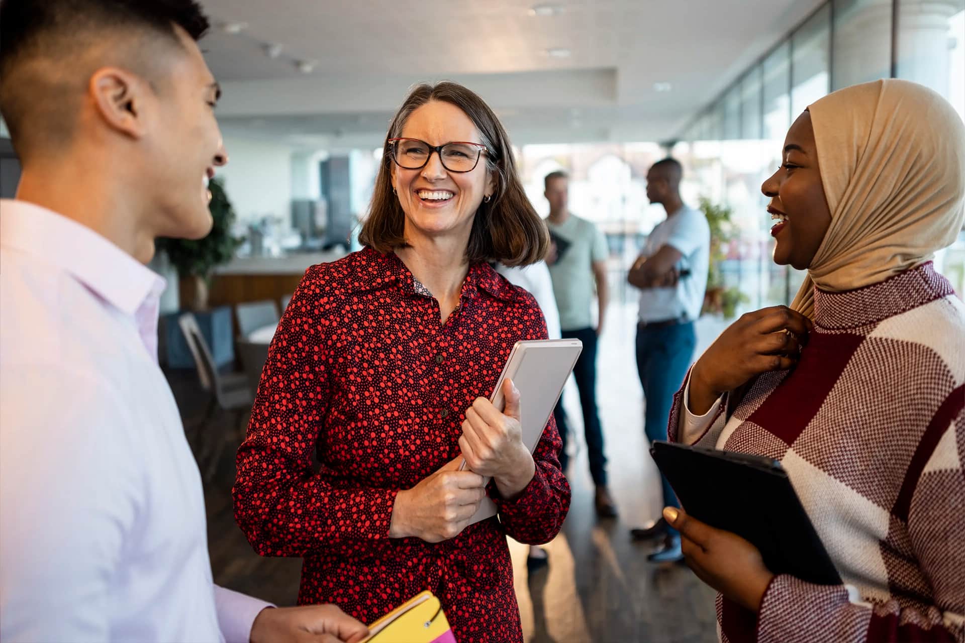 Three colleagues standing, chatting and smiling with each other.