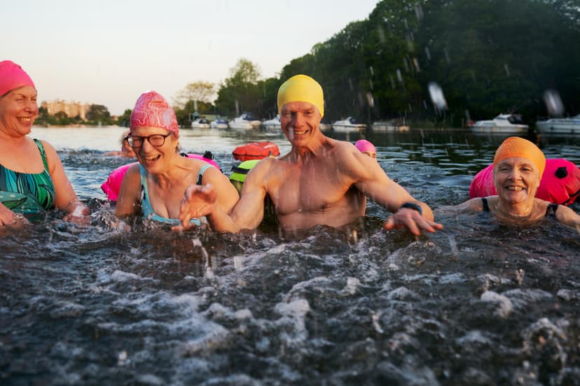 A group of swimmers splashing and playing in water, wearing colourful swimming hats.